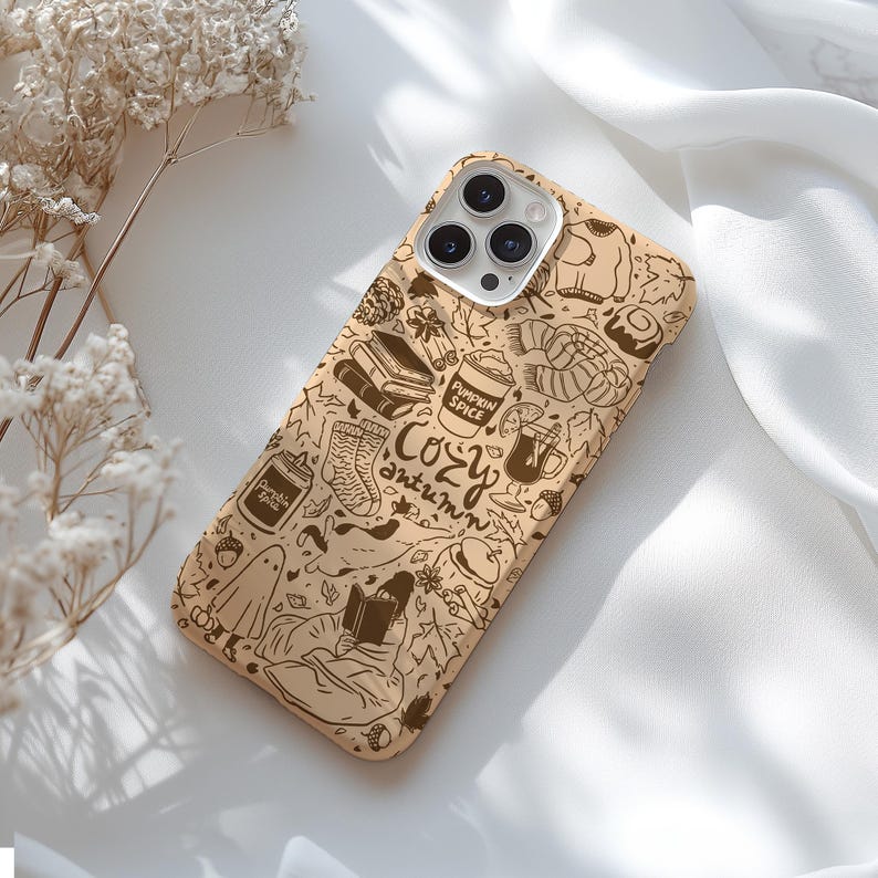May include: A tan phone case with a brown doodle design featuring autumn themes. The case includes illustrations of books, coffee cups, socks, and the words "Cozy Autumn". The case is designed for a smartphone.