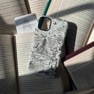 May include: A white smartphone case featuring black line art illustrations of fantasy elements, including a wolf, dragon, books, and the text: Once upon a time there was a girl who loved to read, Death by TBR, Fantasy Book Club, and plot twist.