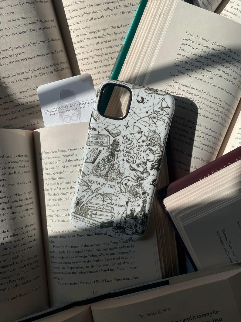 May include: A white smartphone case featuring black line art illustrations of fantasy elements, including a wolf, dragon, books, and the text: Once upon a time there was a girl who loved to read, Death by TBR, Fantasy Book Club, and plot twist.