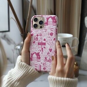May include: A pink iPhone case with a white background and a pink and white design. The design includes hearts, stars, a skeleton, a dice, a bicycle, and the text "18th Avenue" and "Love".