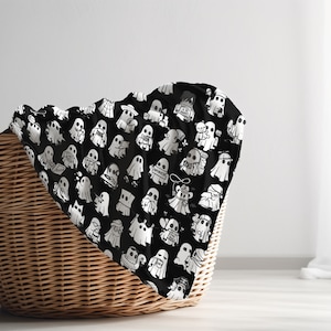 May include: A black and white patterned fabric with a design of many ghosts. The fabric is draped over a wicker basket.