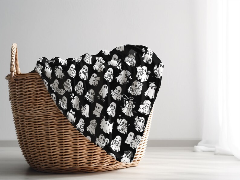 May include: A black and white patterned fabric with a design of many ghosts. The fabric is draped over a wicker basket.