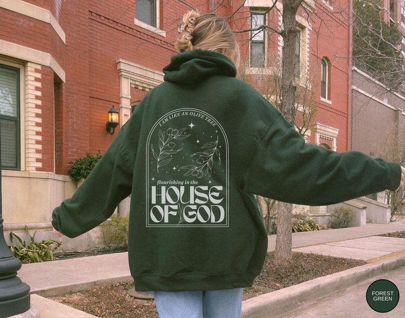 Puede incluir: Una sudadera con capucha verde oscuro con un dise&ntilde;o gr&aacute;fico blanco que presenta un olivo y el texto "Soy como un olivo que florece en la casa de Dios".