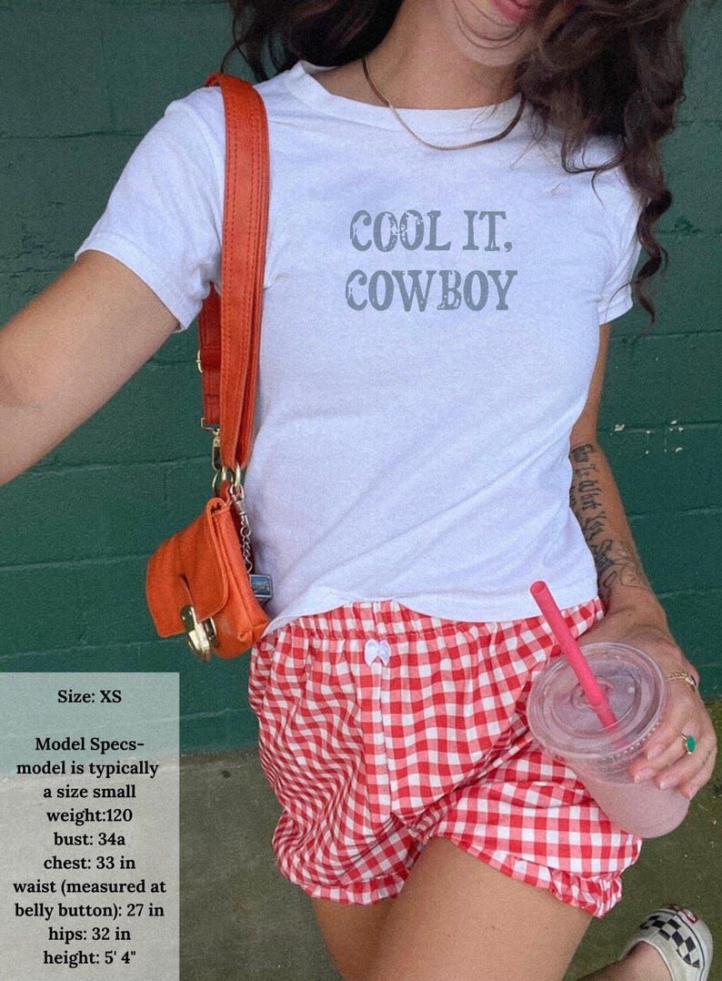 May include: White t-shirt with the text "COOL IT, COWBOY" in gray, paired with red and white checkered shorts. An orange purse and a pink drink with a straw are also visible.
