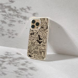 Puede incluir: Una funda transparente para tel&eacute;fono con un fondo beige y un dise&ntilde;o de tem&aacute;tica vaquera en negro. El dise&ntilde;o incluye un sombrero de vaquero, botas, una herradura y las palabras "Howdy", "Cowboy Tears" y "Wild".