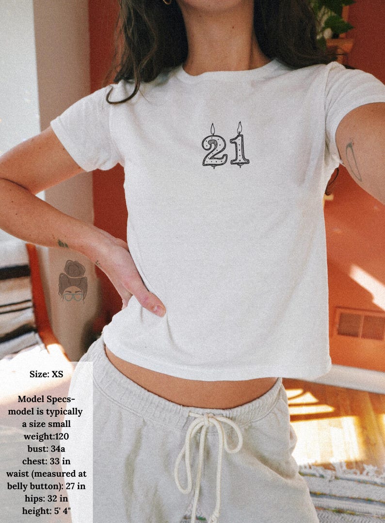 May include: White XS t-shirt with a black graphic of the number 21, styled like a birthday candle. The model's measurements are: bust 34 inches, chest 33 inches, waist 27 inches, hips 32 inches, and height 5' 4".