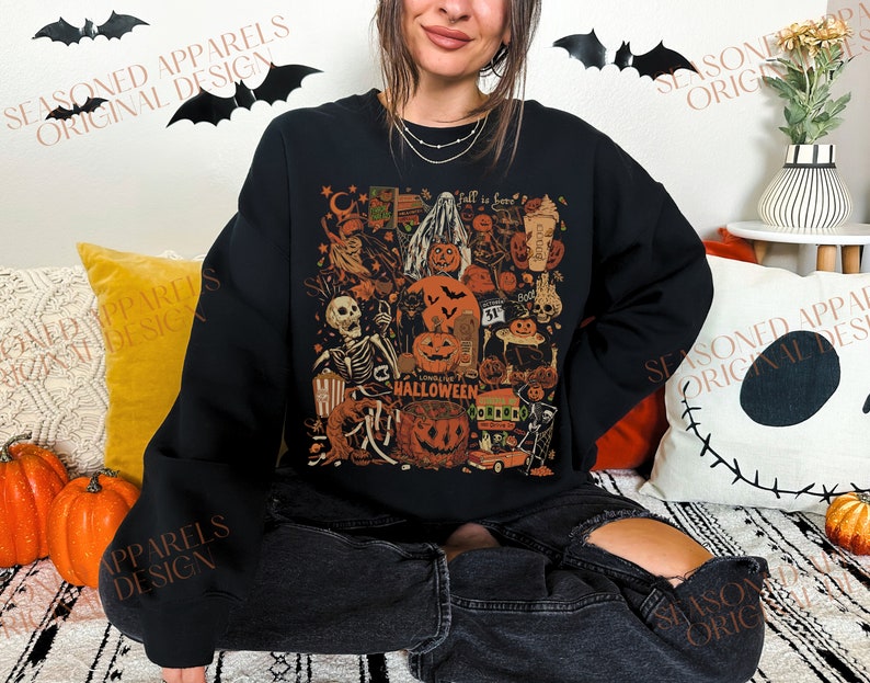 May include: A black sweatshirt with a colorful Halloween-themed graphic print. The print features a skeleton, pumpkins, ghosts, and other spooky elements. The text "Long Live Halloween" is included in the design.
