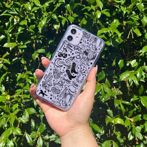 Puede incluir: Funda transparente para tel&eacute;fono con un dise&ntilde;o de tem&aacute;tica vaquera en blanco y negro. La funda presenta ilustraciones de botas de vaquero, un sombrero, herraduras y las palabras "Howdy Cowboy Tears" y "Wild".
