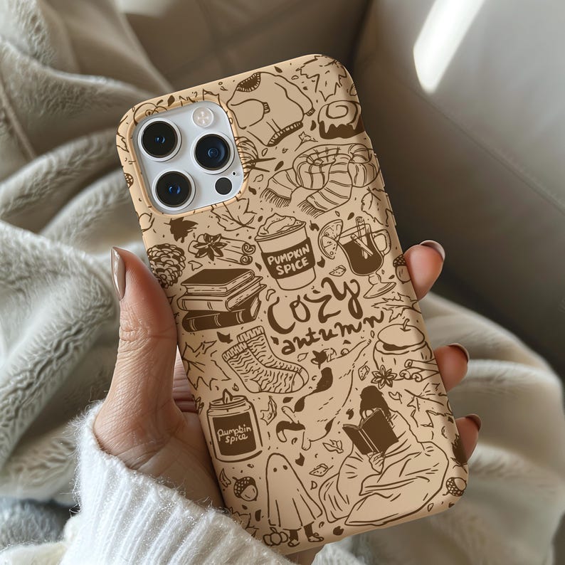 May include: A beige phone case with a brown doodle design featuring autumn-themed illustrations. The case includes images of a sweater, coffee cup, books, socks, and the words "Pumpkin Spice" and "Cozy Autumn".