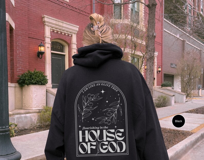 Puede incluir: Sudadera con capucha negra con un estampado gr&aacute;fico blanco de un olivo con el texto "Soy como un olivo que florece en la casa de Dios".