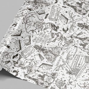 May include: A roll of white wrapping paper with a black fantasy-themed design. The pattern includes dragons, books, stars, and text that reads "Once upon a time there was a girl who loved to read" and "Welcome to the Fantasy Book Club."