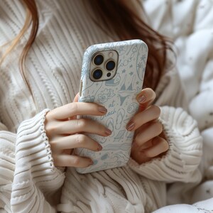 K&ouml;nnte beinhalten: Wei&szlig;es iPhone-Case mit hellblauem Strandmuster. Das Design umfasst Illustrationen von Palmen, einem Bikini, Flip-Flops und dem Text "at the beach". Das Case hat eine gl&auml;nzende Oberfl&auml;che.