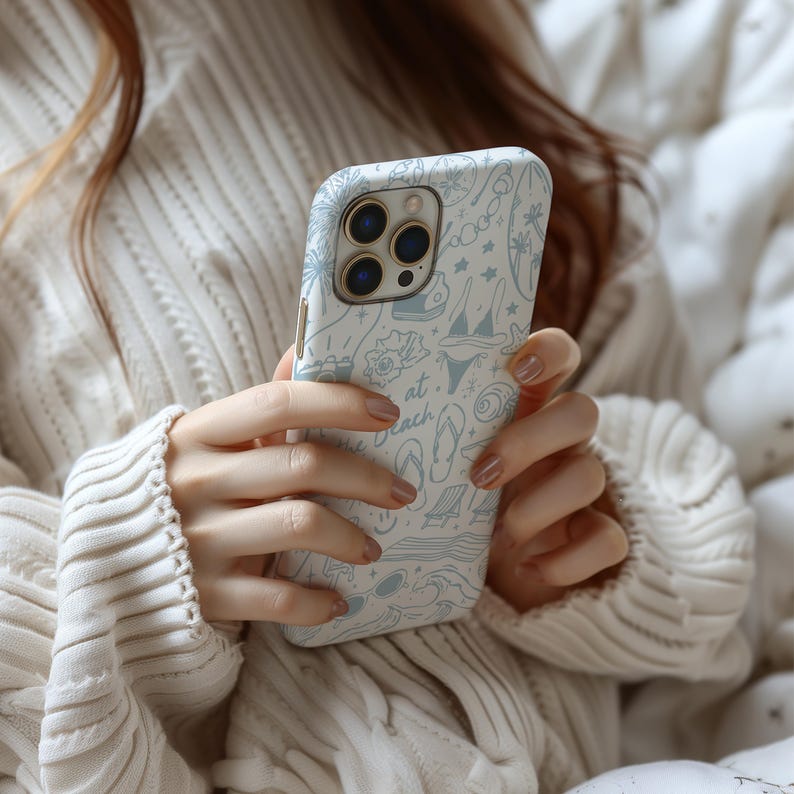 K&ouml;nnte beinhalten: Wei&szlig;es iPhone-Case mit hellblauem Strandmuster. Das Design umfasst Illustrationen von Palmen, einem Bikini, Flip-Flops und dem Text "at the beach". Das Case hat eine gl&auml;nzende Oberfl&auml;che.