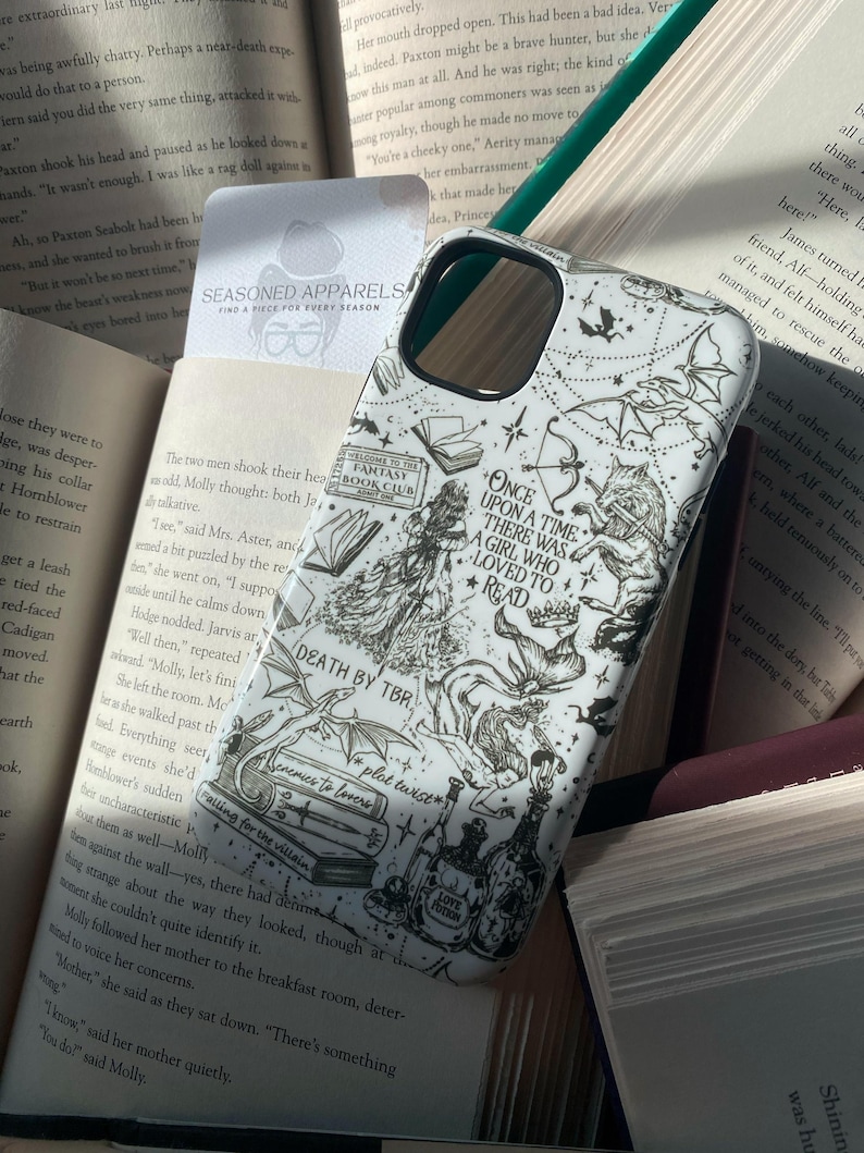 May include: A white smartphone case featuring black line art illustrations of fantasy elements, including a wolf, dragons, books, and potions. The text reads: Once upon a time there was a girl who loved to read, Fantasy Book Club, Death by TBR, and Love Potion.