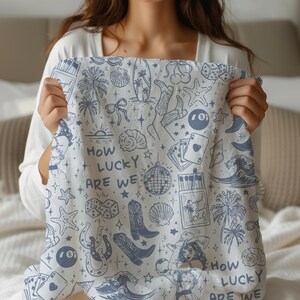 May include: White cotton tea towel with a blue and white pattern of various icons including a horseshoe, a palm tree, a disco ball, a playing card, a surfboard, a seashell, a pair of cowboy boots, and the text "How lucky are we".