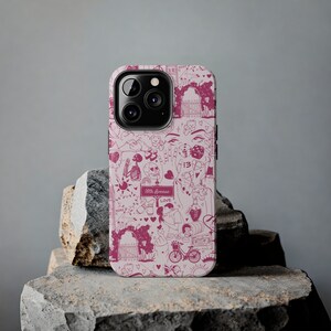 May include: A pink and white iPhone case with a variety of illustrations, including a skeleton, a heart, a dice, a sun, a bicycle, and the text "16th Avenue".