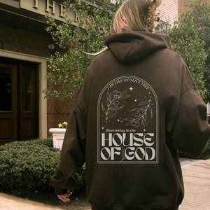 Puede incluir: Una sudadera marr&oacute;n con un gr&aacute;fico blanco en la espalda. El gr&aacute;fico presenta un olivo con el texto "Soy como un olivo que florece en la casa de Dios".