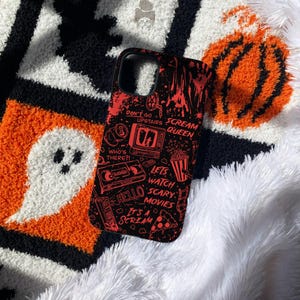 May include: A black phone case featuring a red graphic print of horror movie icons and text including Don't Go Upstairs, Scream Queen, Who's There?, Let's Watch Scary Movies, Hello, and It's A Scream, with illustrations of a television, VHS tape, and popcorn.