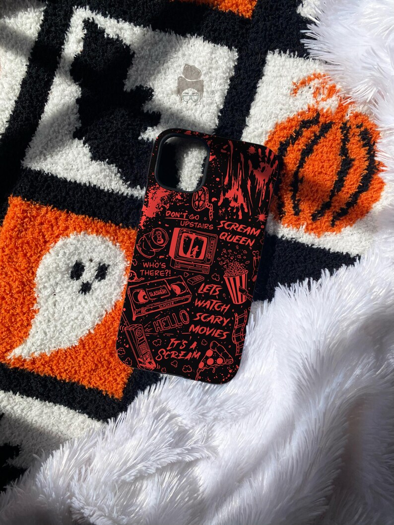 May include: A black phone case featuring a red graphic print of horror movie icons and text including Don't Go Upstairs, Scream Queen, Who's There?, Let's Watch Scary Movies, Hello, and It's A Scream, with illustrations of a television, VHS tape, and popcorn.