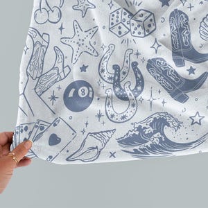 May include: A white fabric with a blue and white pattern of various symbols including a horseshoe, a seashell, a wave, a playing card, a dice, a cowboy boot, a starfish, and a 8-ball.