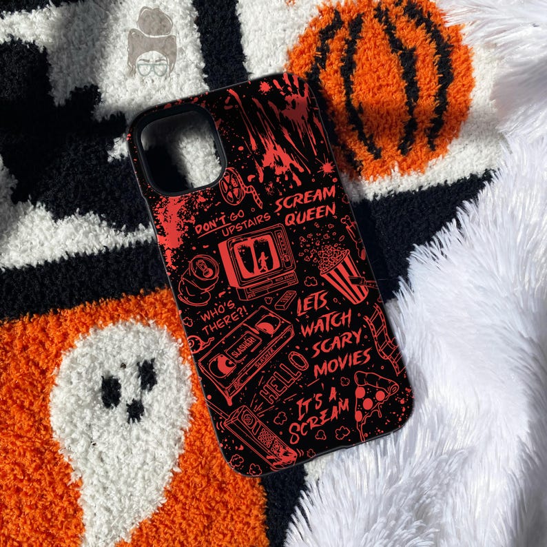 May include: A black phone case featuring a red graphic print of horror movie motifs including a television, a VHS tape, a popcorn bucket, and a slice of pizza. The text reads: Don't go upstairs, Scream Queen, Who's there?, Lets watch scary movies, Hello, It's a scream.