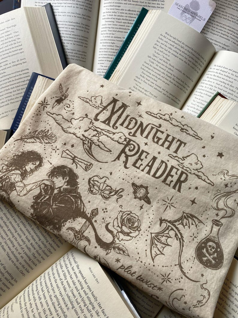 Puede incluir: Un art&iacute;culo de tela beige con ilustraciones serigrafiadas en marr&oacute;n oscuro, incluyendo el texto "MIDNIGHT READER" y "plot twist". El dise&ntilde;o incluye una pareja, una m&aacute;scara, una rosa, un drag&oacute;n, una botella con una calavera, estrellas y nubes.