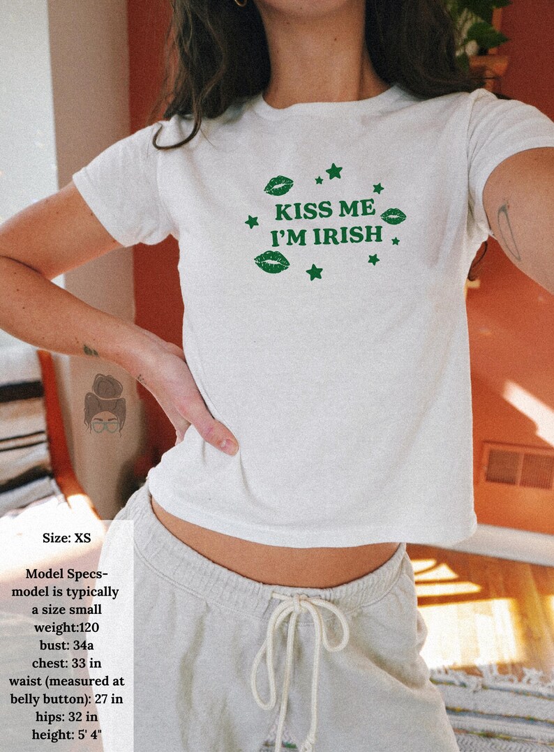 May include: White XS t-shirt with the text "KISS ME I'M IRISH" in green, along with green lips and stars. The model is wearing light gray sweatpants. The model's bust is 33 inches, waist 27 inches, and hips 32 inches.