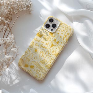 May include: A yellow and white phone case with a beach theme. The case features a variety of beach-related icons, including a sun, flip flops, a beach umbrella, and a seashell. The text "Meet me at the Beach" is printed on the case.