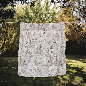 May include: A white throw blanket with a black and white print of books, dragons, and other fantasy elements. The text on the blanket reads "Once upon a time there was a girl who loved to read" and "Death by TBR".