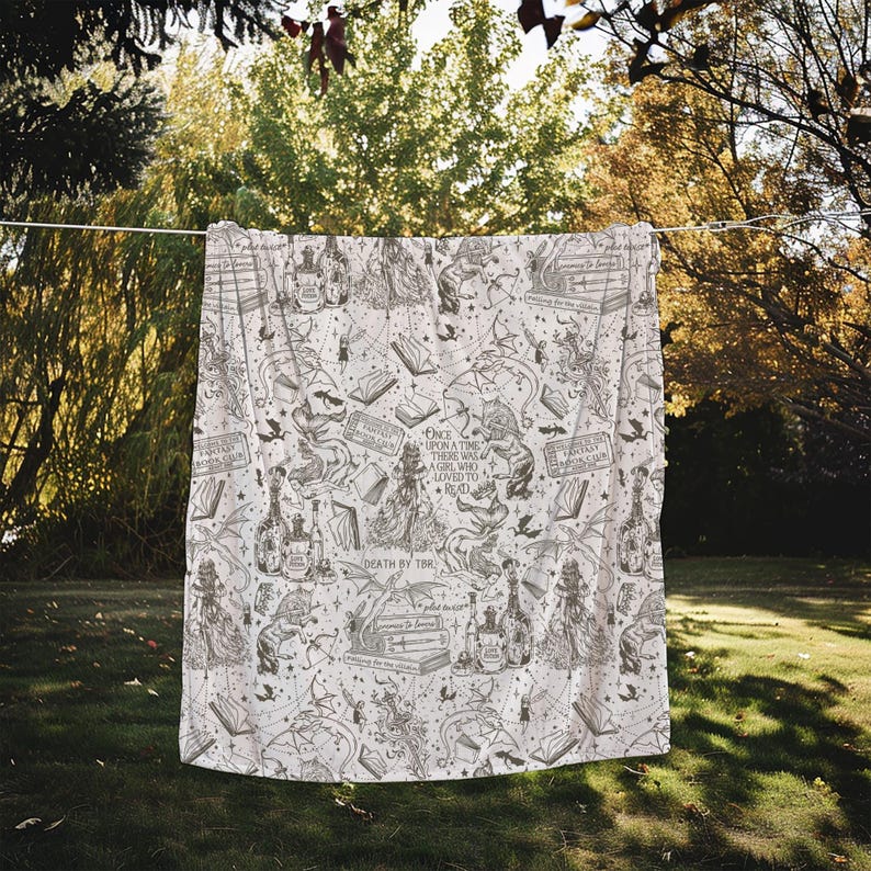 May include: A white throw blanket with a black and white print of books, dragons, and other fantasy elements. The text on the blanket reads "Once upon a time there was a girl who loved to read" and "Death by TBR".