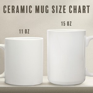 K&ouml;nnte beinhalten: Zwei wei&szlig;e Keramikbecher, einer mit 11 oz und einer mit 15 oz, nebeneinander auf einem Regal. Die Becher sind leer und bereit f&uuml;r die Personalisierung.