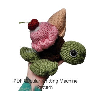 Könnte beinhalten: Ein gestricktes Schildkrötenspielzeug mit einem braunen Panzer, der mit einer rosa Eiskugel, einer beigen Waffel und einer kleinen roten Kirsche verziert ist. Der Text lautet: PDF Circular Knitting Machine Pattern 22 and 48. Die Schildkröte hat einen grünen Kopf.