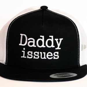 May include: Black and white trucker hat with a white embroidered phrase "Daddy issues" on the front.