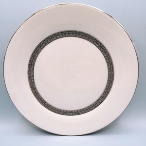 May include: White ceramic dinner plate with a black and gold decorative border.