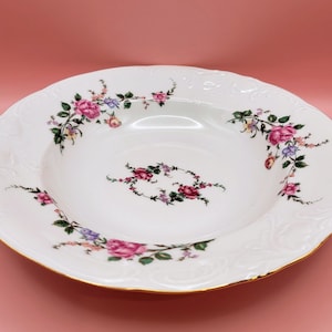 May include: White porcelain soup bowl with a floral design featuring pink, purple, and yellow flowers. The bowl has a gold rim and a raised, textured edge.