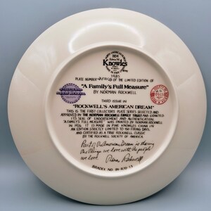 Puede incluir: Un plato de cer&aacute;mica blanco con un borde dorado y una imagen impresa de una familia. El plato forma parte de la serie "Rockwell's American Dream", autenticado por el Norman Rockwell Family Trust. El n&uacute;mero del plato es 2501B y el texto "A Family's Full Measure" est&aacute; impreso en el plato.