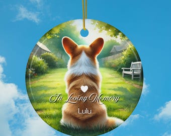 May include: A round ceramic ornament featuring a brown and white corgi dog looking away from the viewer. The dog is in a green grassy field with a small white heart on its back. The text "In Loving Memory Lulu" is printed below the dog.