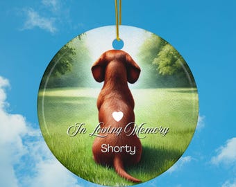 May include: A round ceramic ornament featuring a brown dachshund sitting in a green field with a white heart on its back. The text "In Loving Memory Shorty" is printed below the dog.