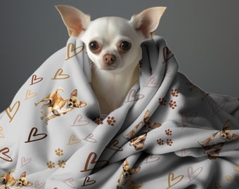 May include: A white chihuahua dog is curled up in a gray fleece blanket with a brown heart pattern. The blanket is covered in small brown paw prints and hearts.
