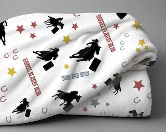 May include: White fleece blanket with a repeating pattern of black silhouettes of horses and riders, red and yellow stars, and the text "Barrel Blastin' Bliss" and "Turn and Burn".