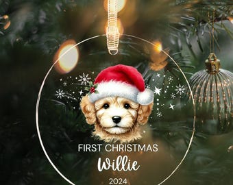 May include: A clear glass Christmas ornament with a white background and a cute dog wearing a red Santa hat. The ornament says "First Christmas Willie 2024".