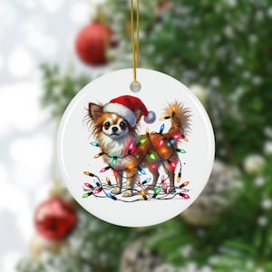 May include: A round Christmas ornament featuring a Chihuahua wearing a Santa hat and wrapped in colorful Christmas lights. The dog has brown and white fur. A gold string is attached for hanging. Festive holiday decor.