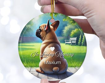 May include: A round ceramic ornament featuring a brown and white French Bulldog sitting in a green grassy field. The ornament has the text "In Loving Memory Maximum" on it.
