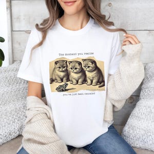 May include: White t-shirt with a humorous image of three kittens and a frog. The text reads "The moment you realize... you've just been canceled."