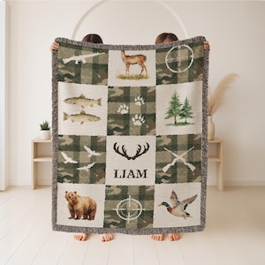 May include: A woven throw blanket with a camouflage and cream-colored square pattern. The squares feature images of a deer, fish, bear, birds, trees, antlers, footprints, crosshairs, and guns. The name "Liam" is printed on the blanket.
