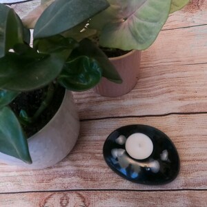 Peut inclure: Un bougeoir ovale noir et blanc moucheté avec une bougie chauffe-plat blanche à l'intérieur. Le bougeoir est posé sur une surface en bois.