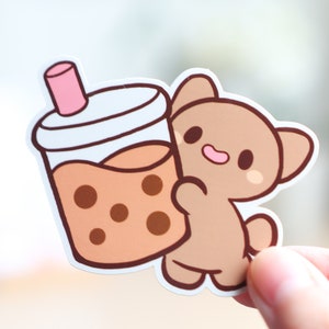 May include: A brown cartoon bear holding a brown and white boba tea cup with a pink straw.