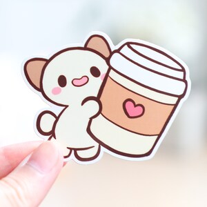 May include: A white cartoon animal with brown ears holding a brown and white coffee cup with a pink heart on it.