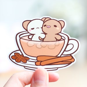 May include: A white and brown cartoon animal couple is sitting in a teacup with a cinnamon stick and star anise on a saucer.