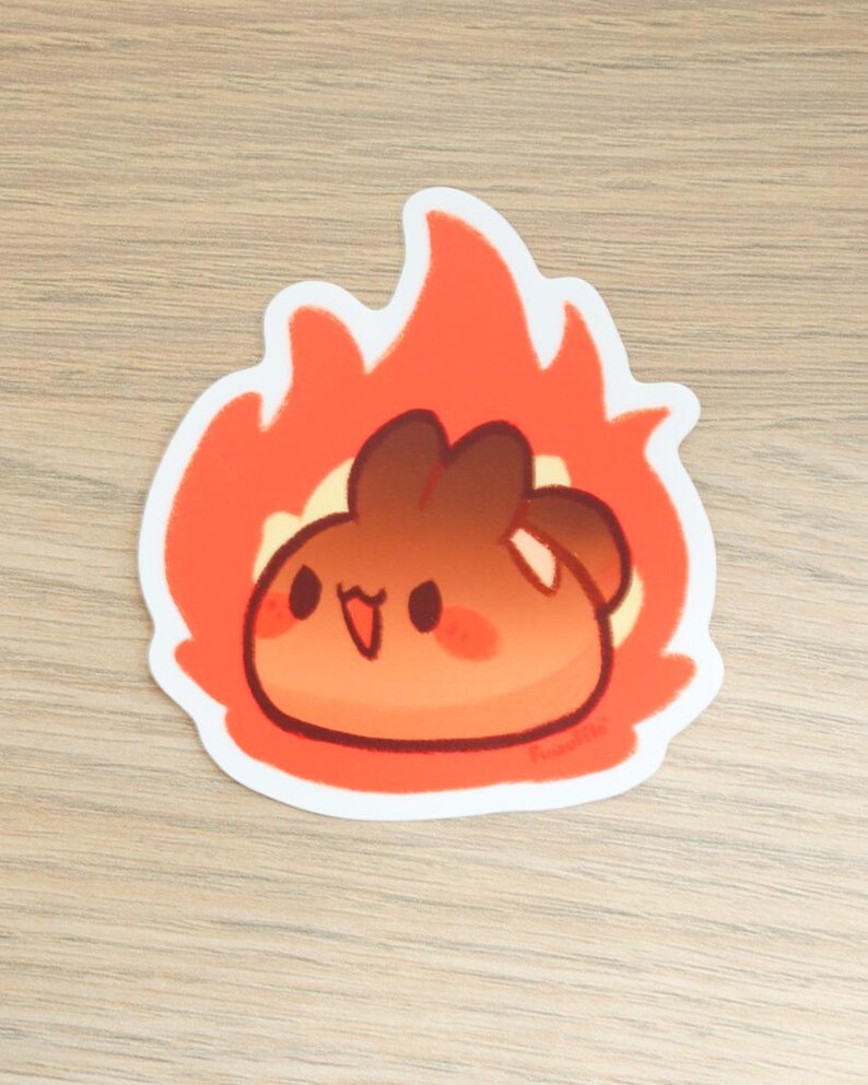 May include: A cartoon sticker of a brown and orange blob with a happy face, surrounded by orange flames. The sticker has a white border and the artist's signature in the bottom right corner.